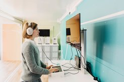 Eine Person trägt Kopfhörer und arbeitet an einem Computer mit Monitor in einem modernen Raum.